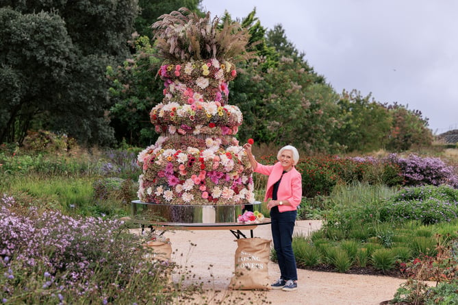 Dame Mary Berry dodges the showers whilst adding the final touches to the giant floral cake